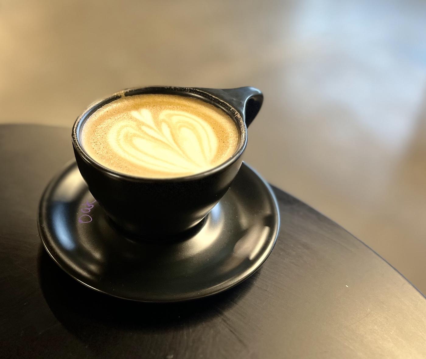 Latte art in a matte black cup and saucer on a black table.