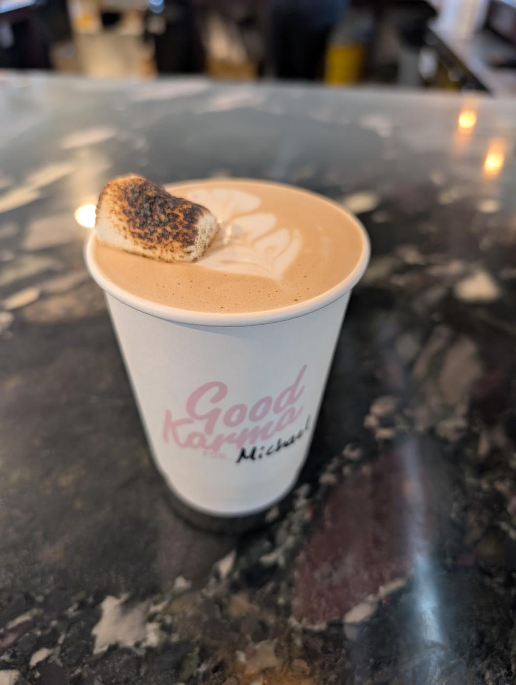 A Good Karma cup, their name in pink brush script, holding a latte topped with a toasted marshmallow.