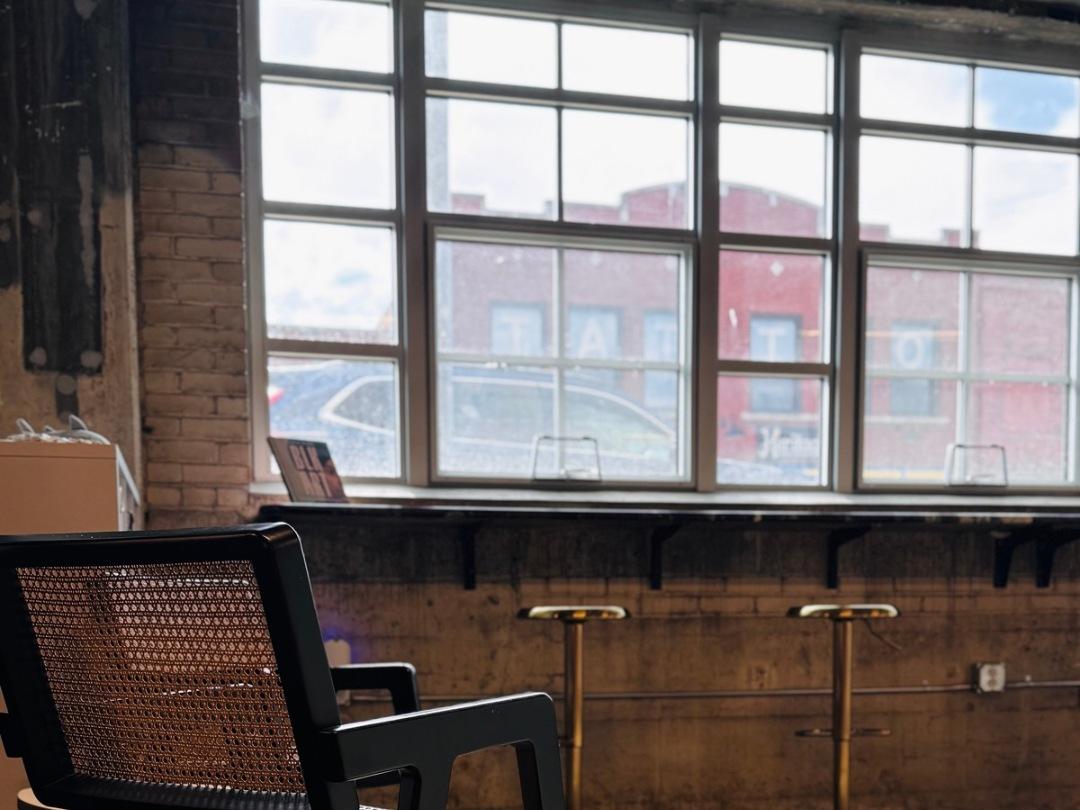 A black cane chair beside the steel framed windows, with gold barstools at the window counter.